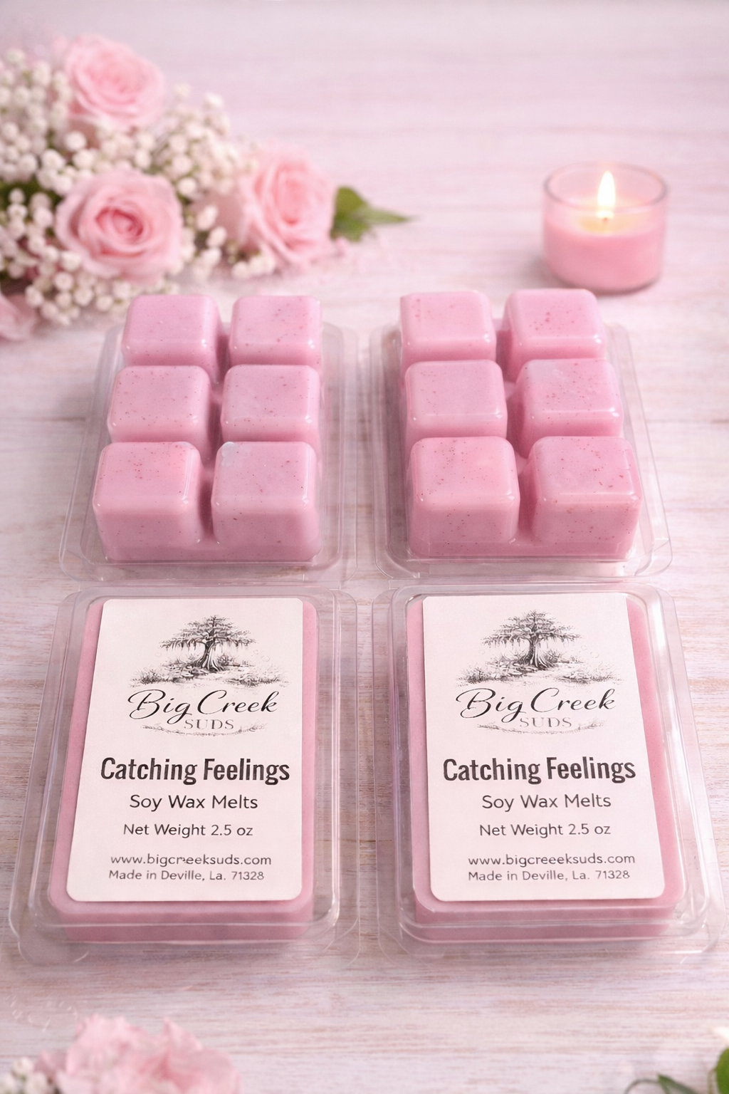 Pink wax melts in packaging with a lit candle and pink flowers on a light wooden surface.