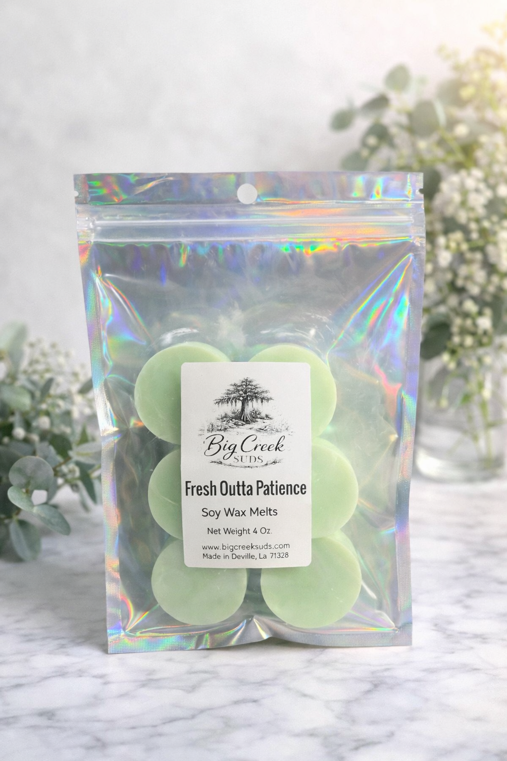 Pack of soy wax melts with a holographic bag on a marble surface with eucalyptus leaves in the background.
